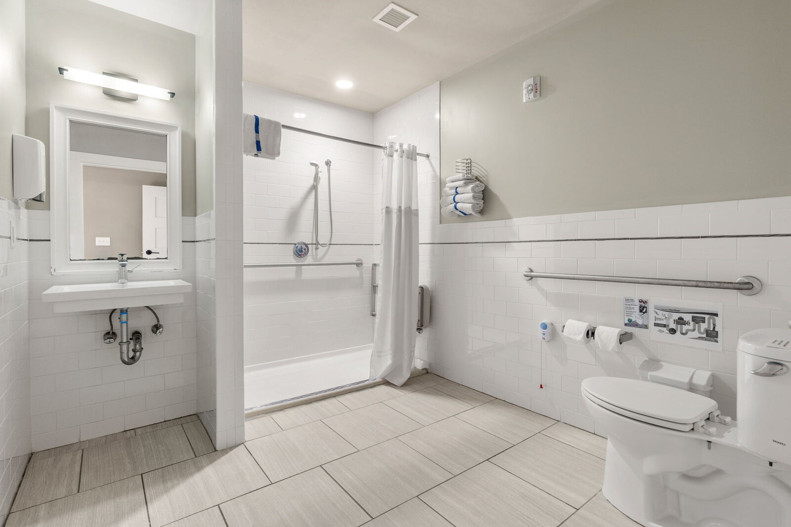 White tiled bathroom with a walk-in shower and grab bars